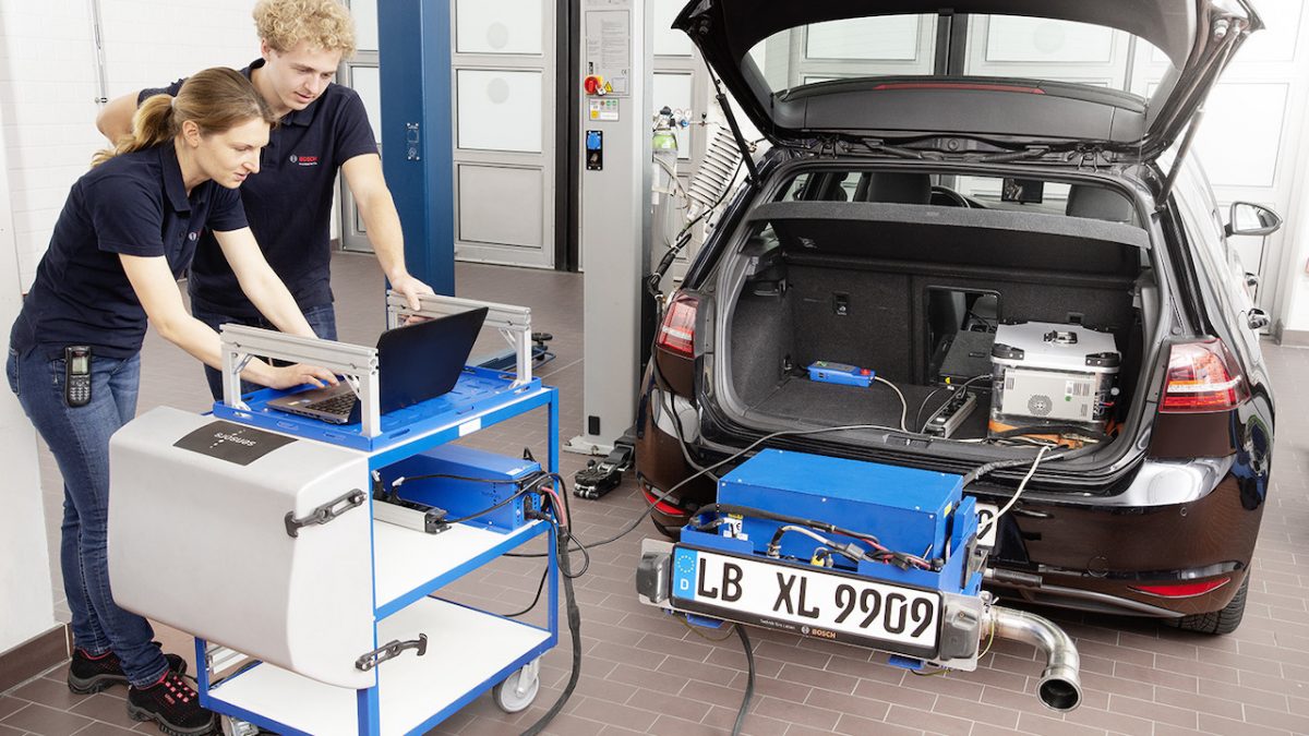A man and woman use a computer beside a car